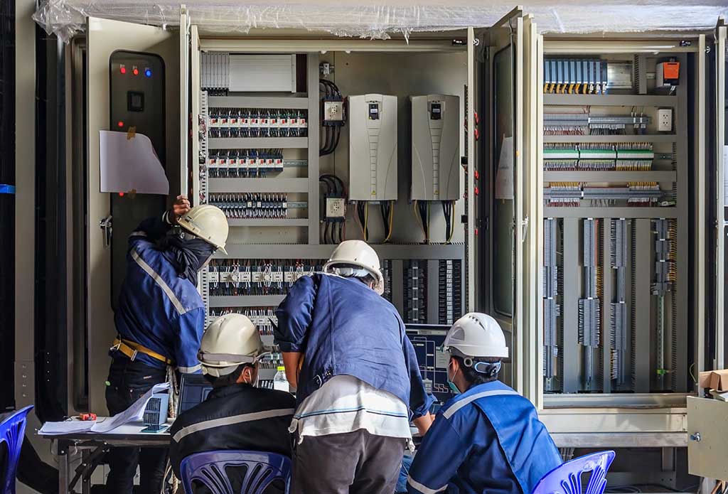 Tres hombres con cascos trabajando en un panel electrónico de gran tamaño