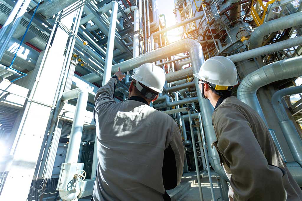 Dos hombres con cascos de seguridad observando tuberías en una planta industrial